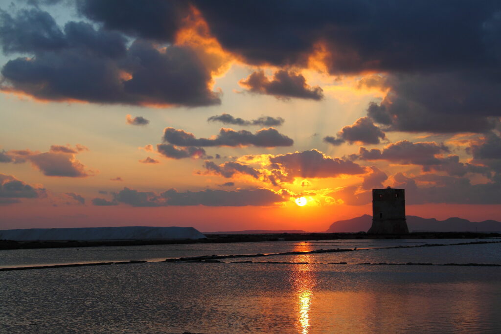 Tramonto di fuoco sulle vasche di sale e sulla torre storica durante il tour saline Trapani Marsala con autista privato.